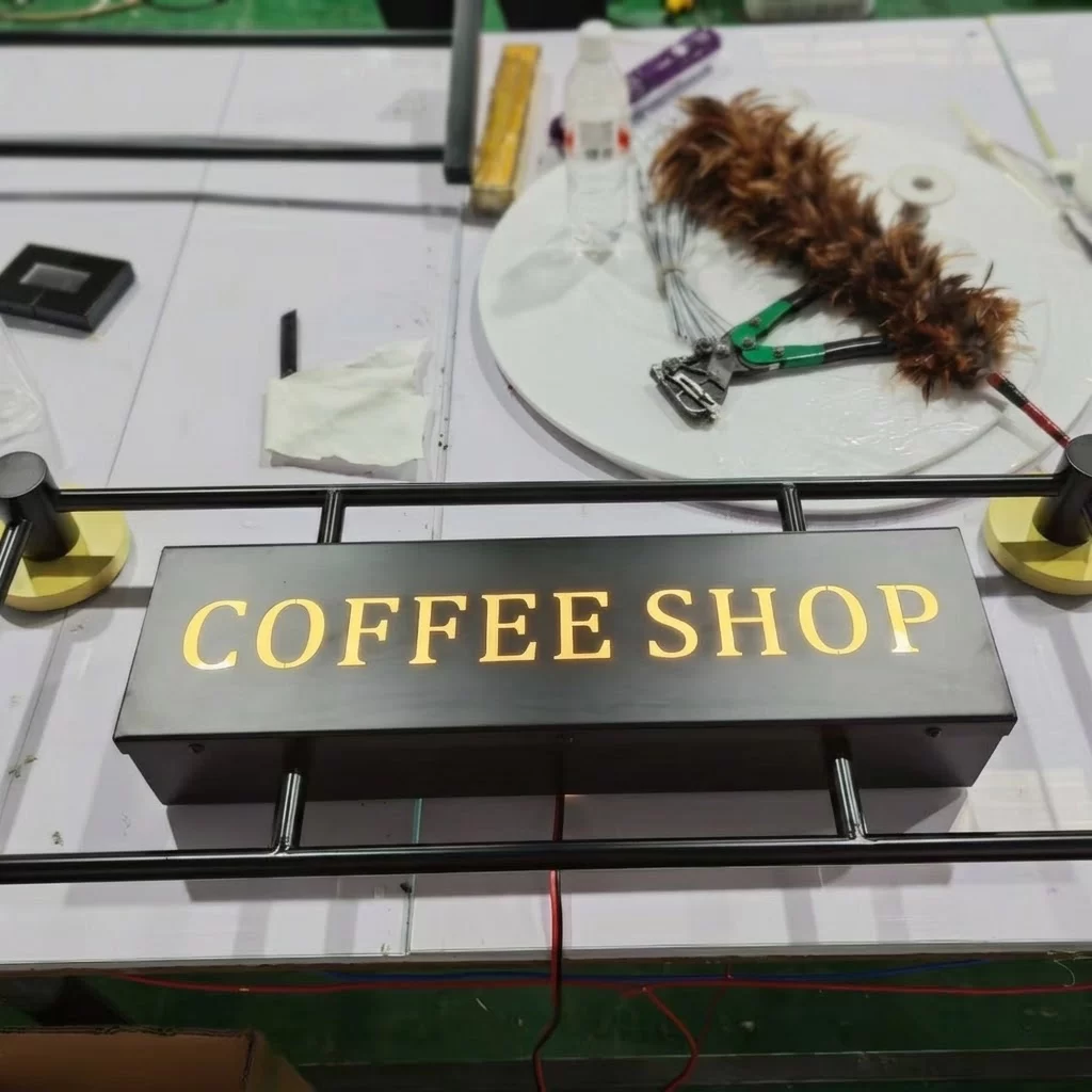 Black powder-coated metal sign box with illuminated LED lettering and brass wall bracket